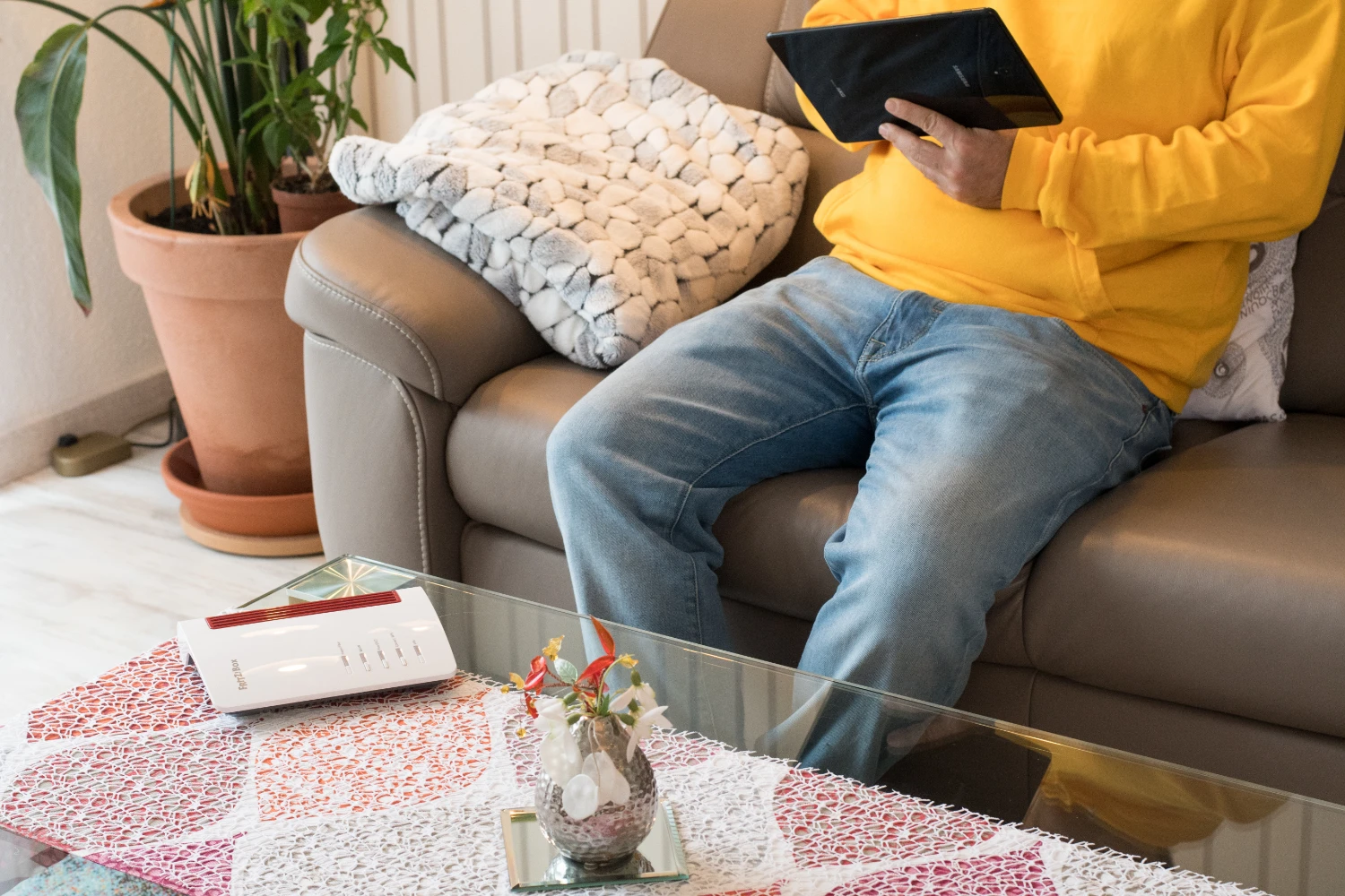 Person mit Tablet im Wohnzimmer neben einem Glasfaserrouter.